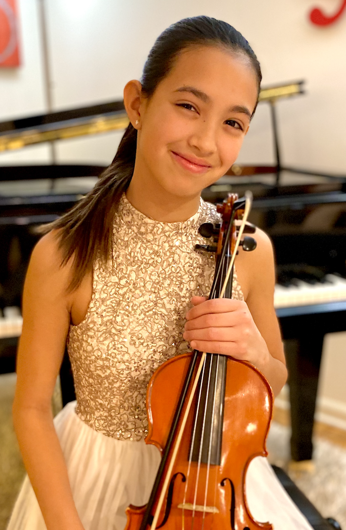 Luciana Velez, holding her violin, in recital dress