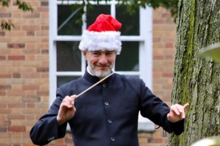 Rossen Milanov in front of a brick building, smiling and wearing a Santa Hat while conducting