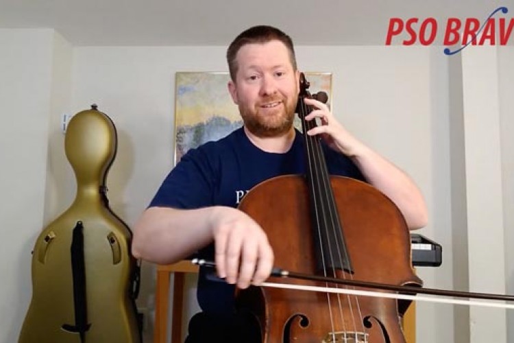 Alistair MacRae smiling at the camera and playing the cello. In the background is a gold cello case. The words PSO BRAVO! are displayed in the top right corner of the image.