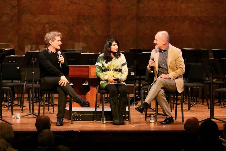 Three people sitting on stage having a discussion together with an audience. 