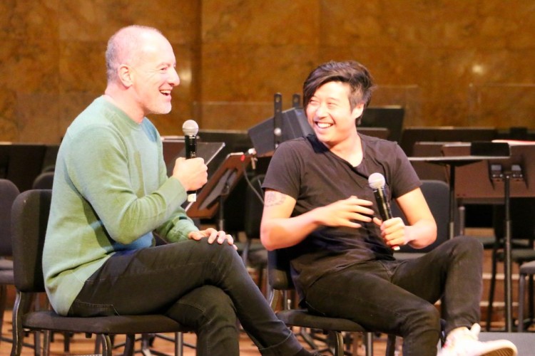 Two people chatting on stage and smiling, both holding microphones. 