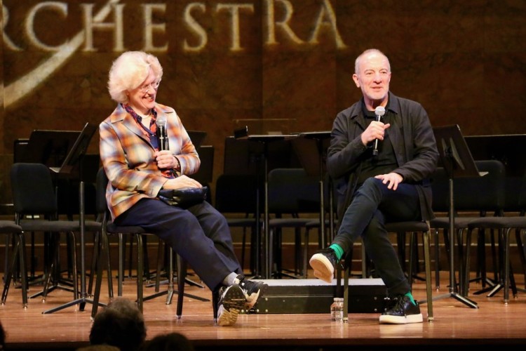 Two people chatting on stage and smiling, both holding microphones.