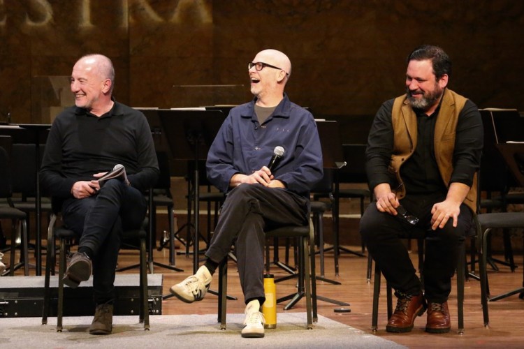Three people men sitting on stage and laughing together.