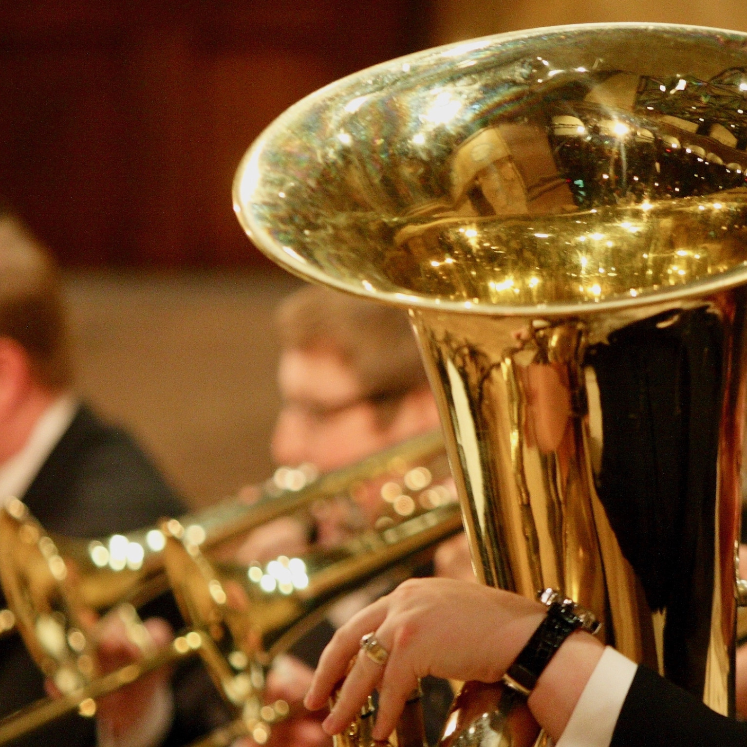 PSO Brass instruments being played by musicians whose faces are blurred in the background.