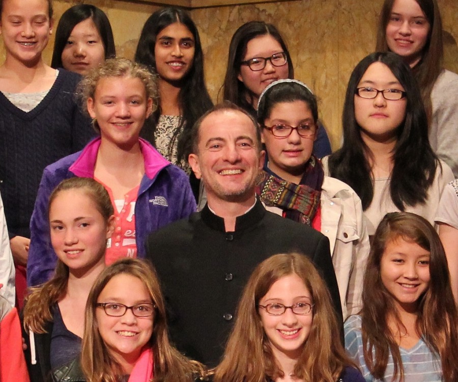 Rossen Milanov stands amid middle school students on stage risers.