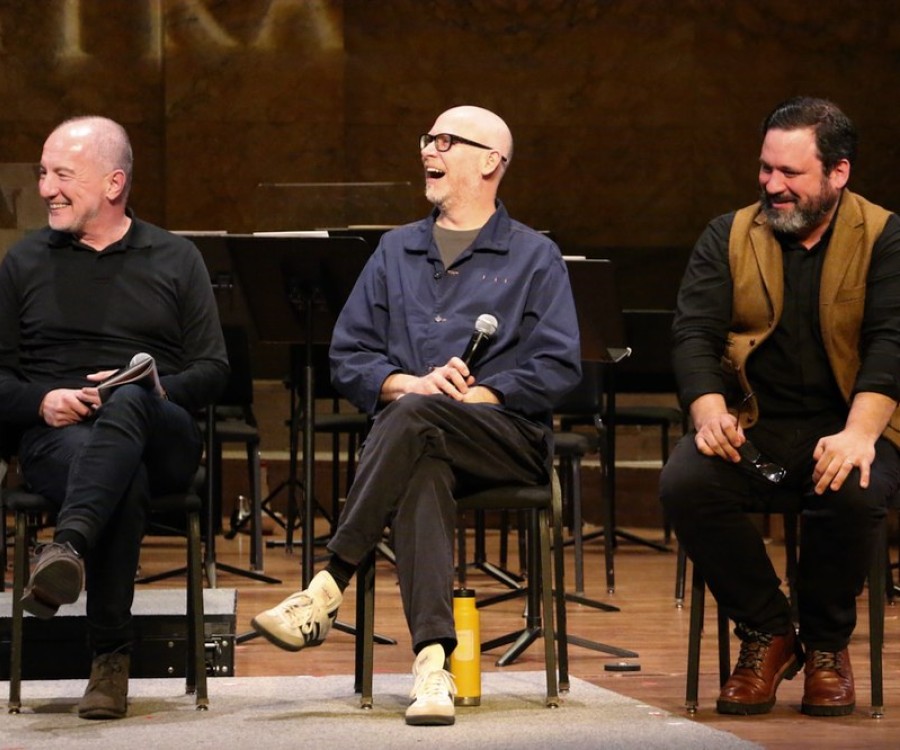 Three men sitting on stage and laughing during a talk.