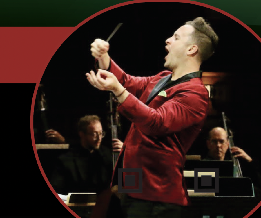 Holiday POPS! conductor John Devlin in action, wearing a red velvet dinner jacket in front of orchestra musicians.