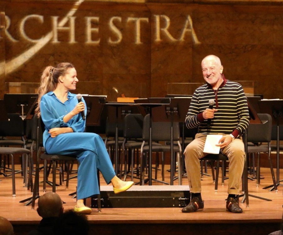Violinist Aubree Oliverson and Maestro Rossen Milanov, seated onstage with microphones in front of an audience.