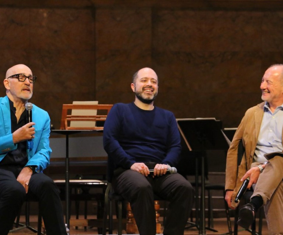 Three men sit on stage and talk in front of an audience. 