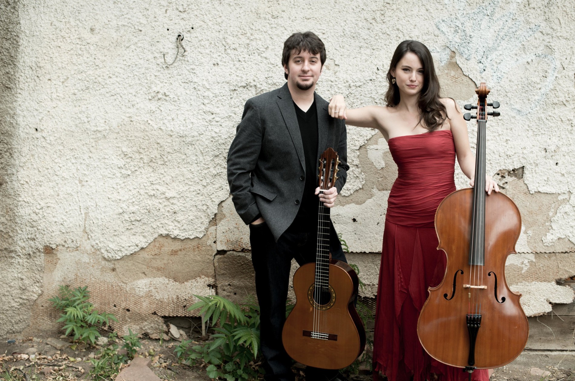 Patrick Sutton, guitar and Kimberly Patterson, cello, outside by a chipped stucco wall.