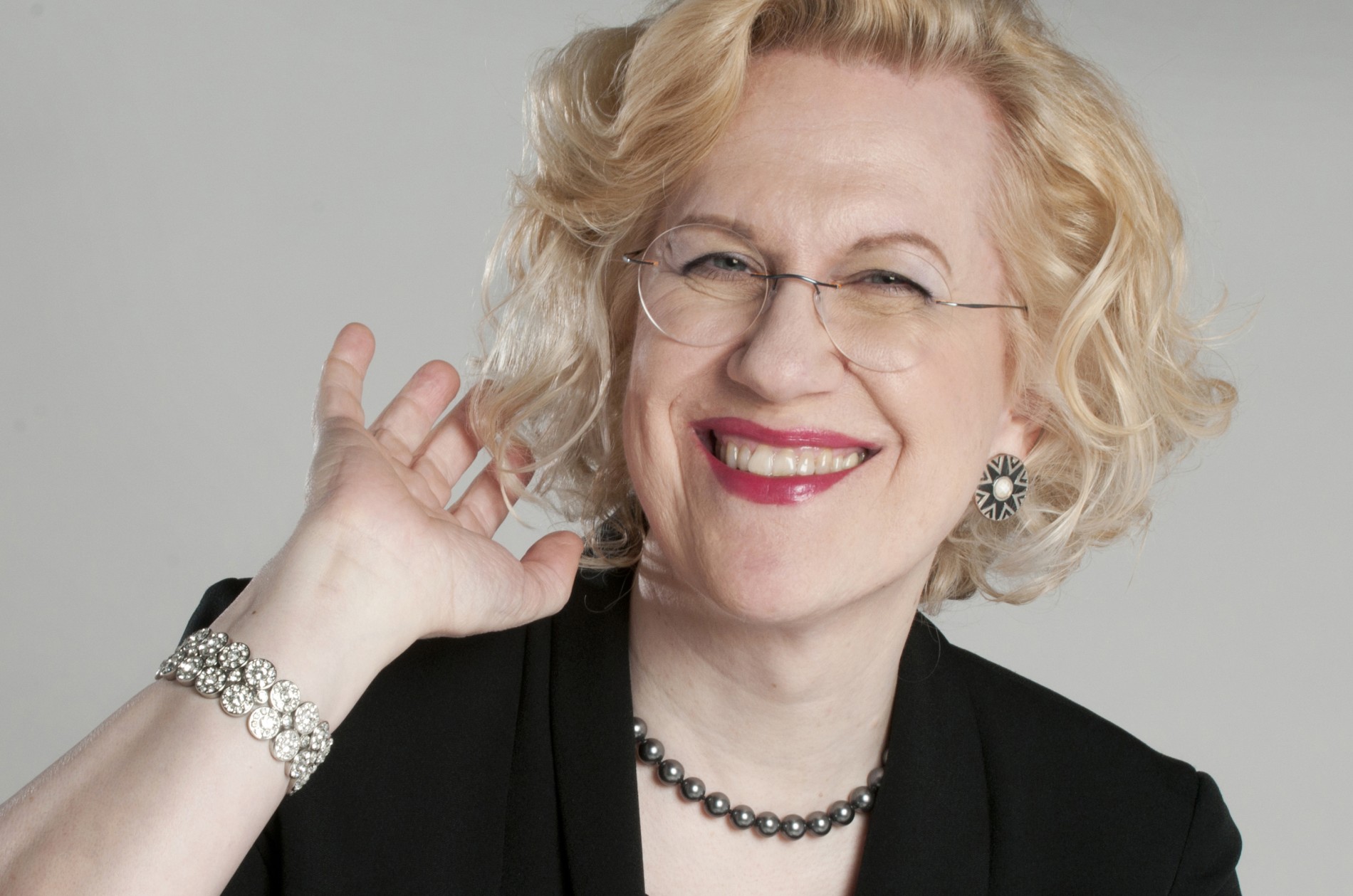 Sara Davis Buechner, pianist, wearing black and smiling with one hand raised to her hair.