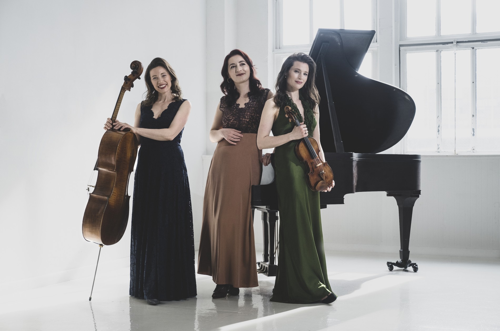 The Claremont Trio - three musicians in gowns with piano, cello, and violin in an all-white room.