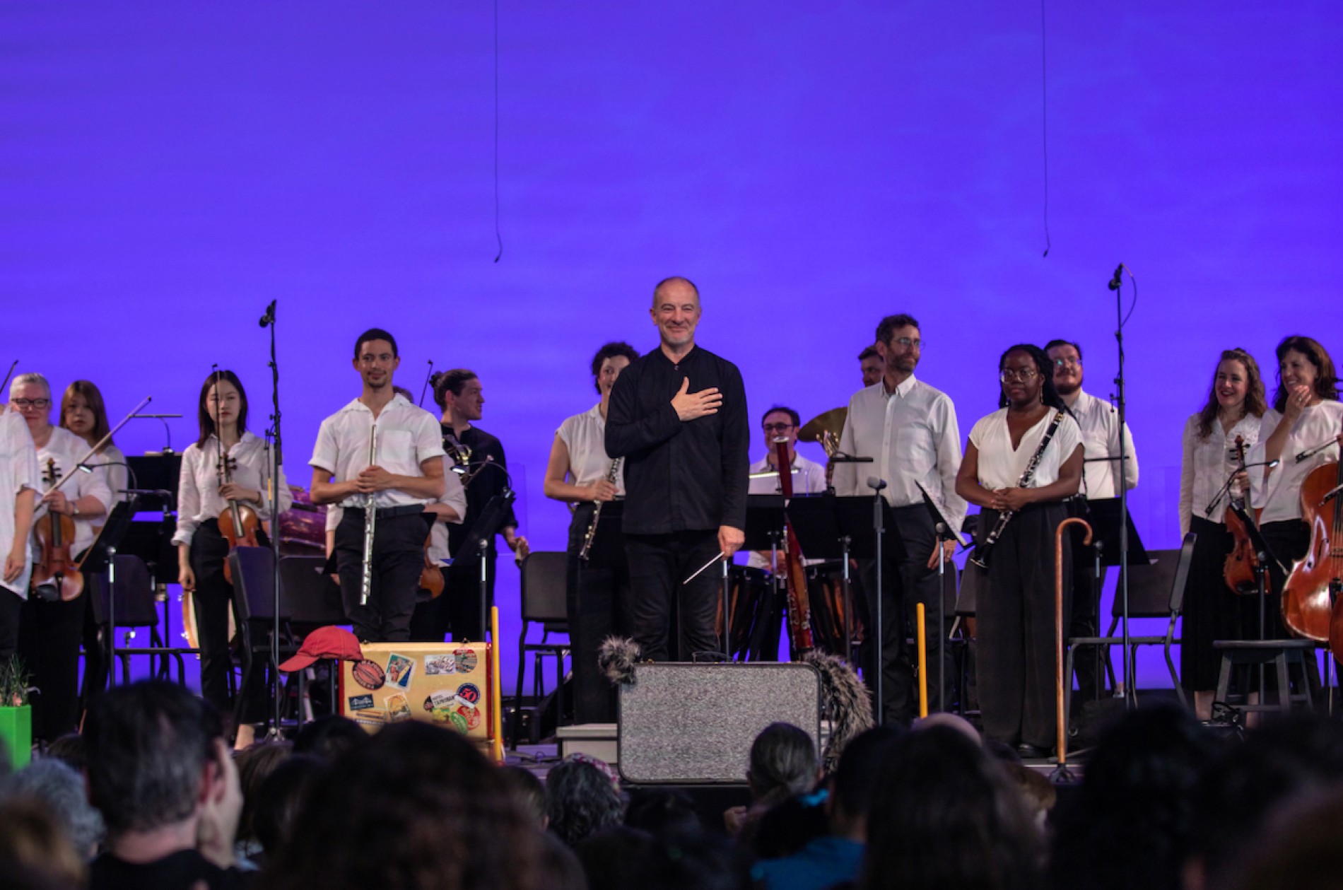 Conductor and orchestra musicians standing and acknowledging an audience members following a performance.