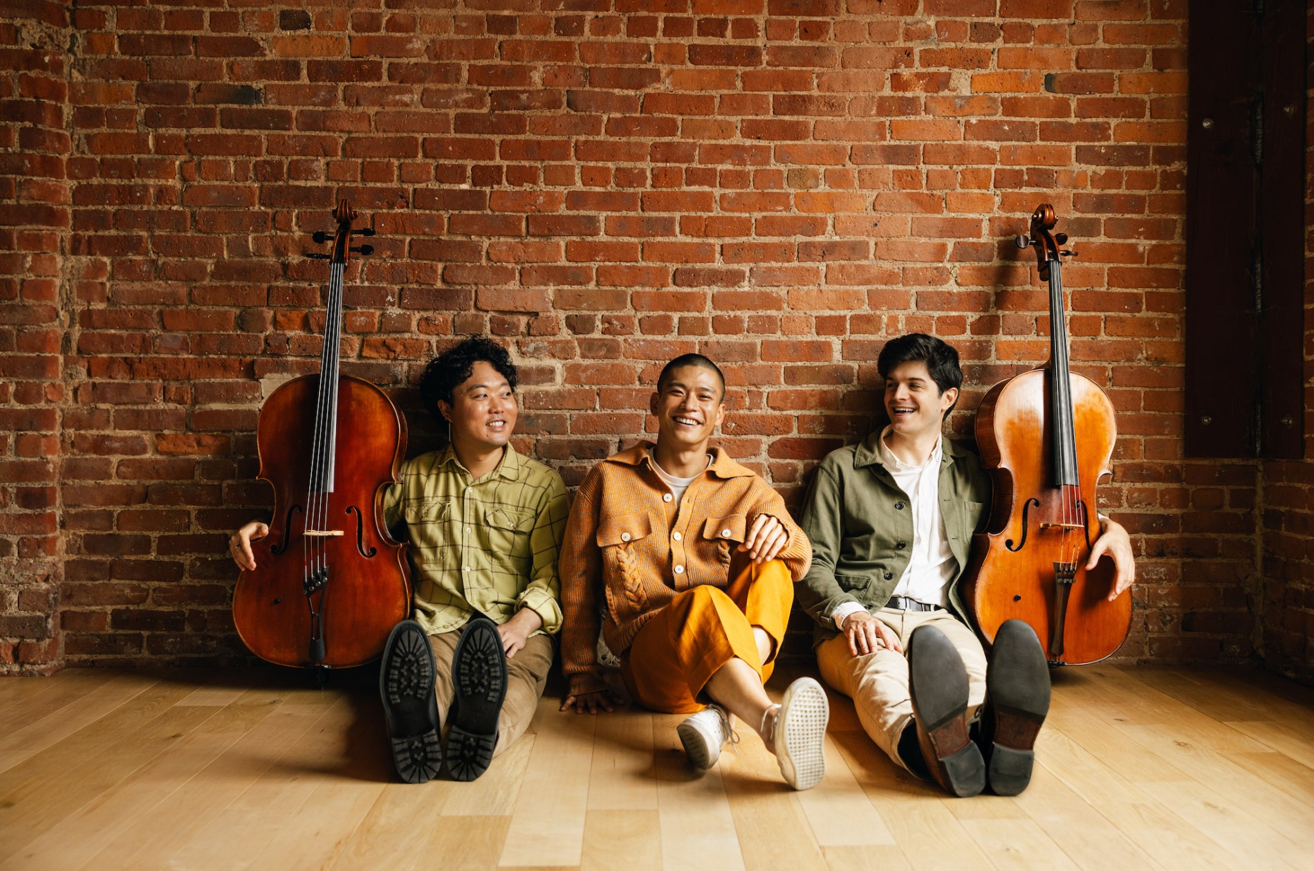 Empire Wild publicity photo: two cellists on either side of a third musician, all seated, posed, on the floor.