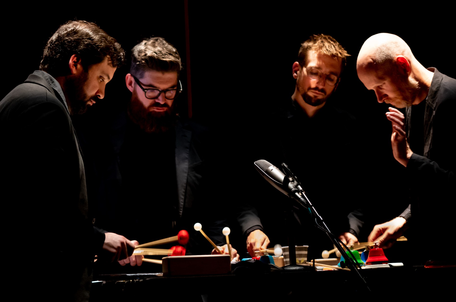 Four percussionists on a darkened stage performing with colorful mallets.